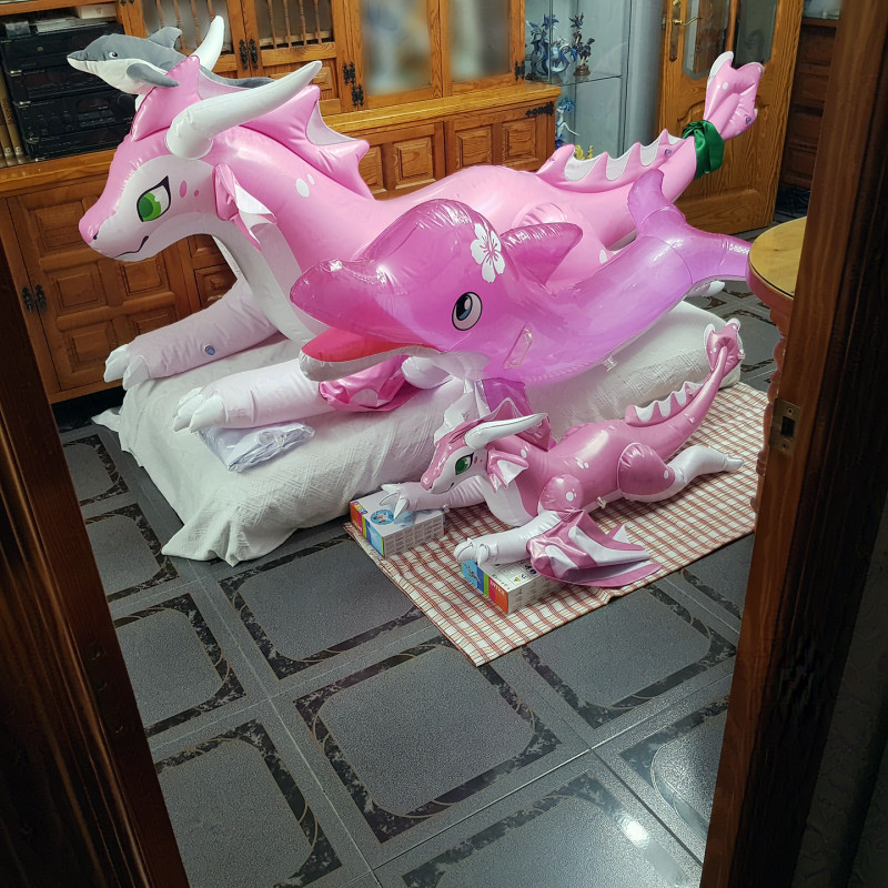 A photo of three inflatable toys (Cerisey, mini-Cerisey, and a pink Josie dolphin) laying together. The dragons are holding three additional dolphins, uninflated. An Ikea dolphin plush is perched on top of Cerisey's head, looking menacingly at the camera.